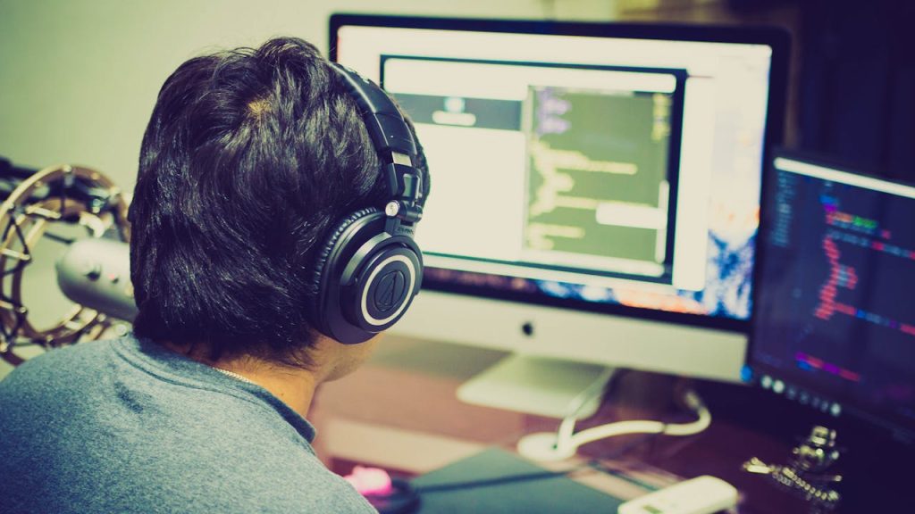Mastering the First Impression: Your intriguing post title goes here A programmer with headphones focuses on coding at a computer setup with dual monitors.